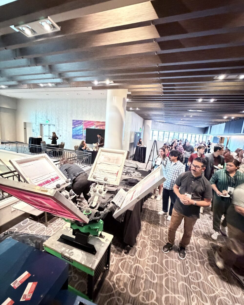 A crowd of guests gathered around a live printing station watching garments being pressed